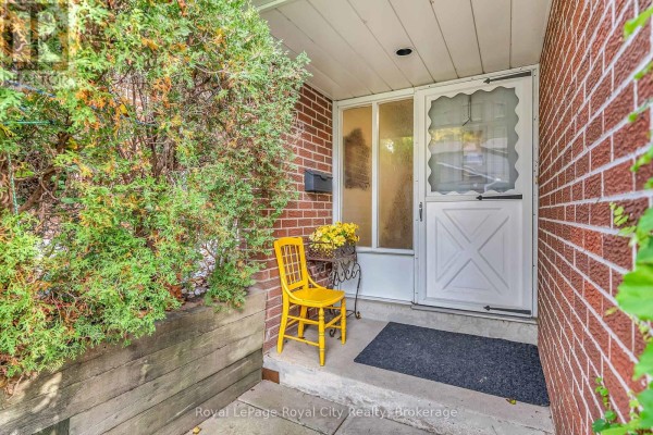 Entrance to a townhouse with a red brick exterior, white door, and a yellow chair. - 52 - 16 Hadati Road, Guelph