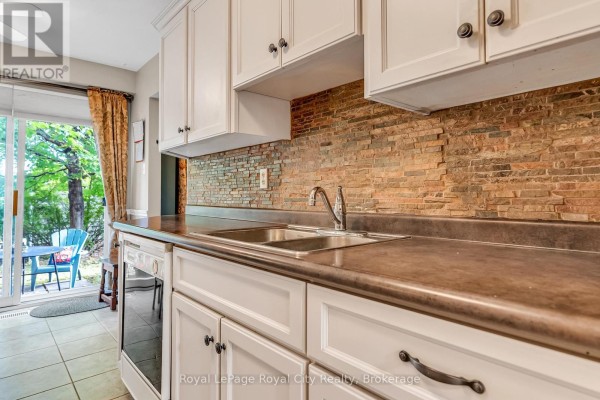 Close-up of a kitchen sink, brown countertop, and a textured stone backsplash. - 52 - 16 Hadati Road, Guelph