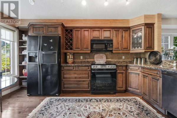 Kitchen with dark wood cabinets, black appliances, granite countertops, and a patterned rug. - 52 - 3480 Upper Middle Road, Burlington