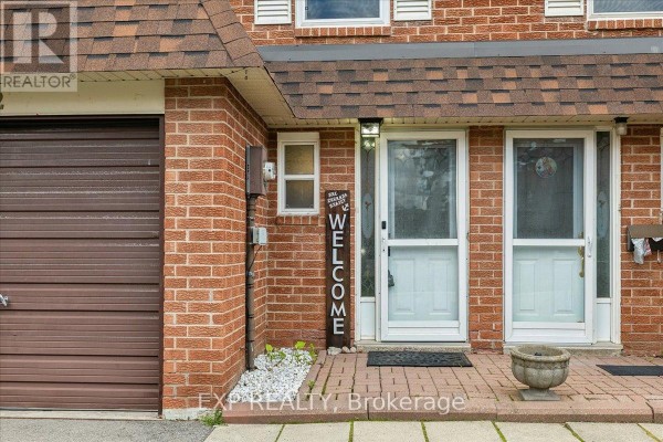 Close-up of townhouse entrance with two white doors, brown garage door, and welcome sign. - 52 - 371 Bronte Street S, Milton