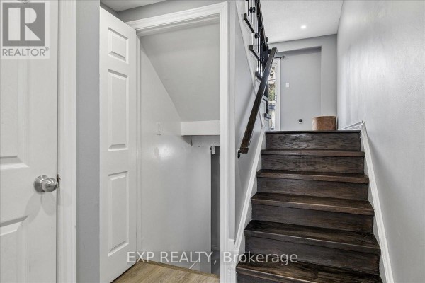 Interior view showing a dark wood staircase with black railing, white door, and grey walls. - 52 - 371 Bronte Street S, Milton