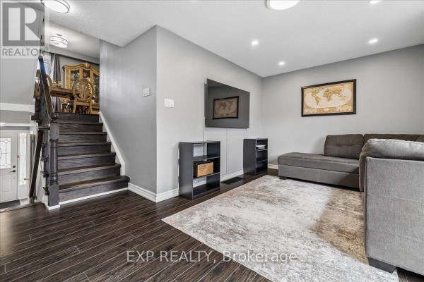 Living room with dark wood floors, grey walls, sectional sofa, rug, and television on wall. - 52 - 371 Bronte Street S, Milton