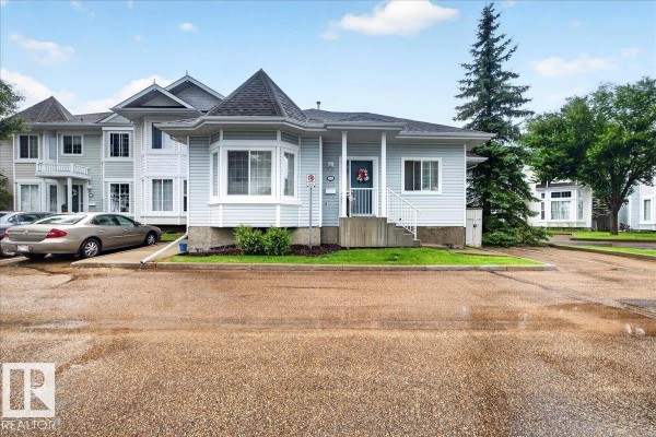 Exterior view of a light blue duplex with a bay window and trees on a cloudy day. - #52 1780 Glastonbury Bv Nw, Edmonton