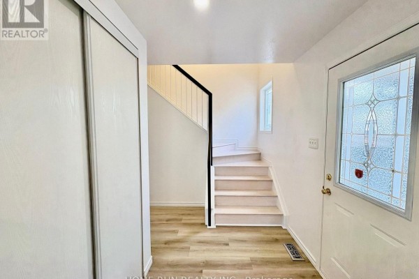 Interior entryway with a white door, mirrored closet doors, and a staircase with white railings. - 52 Collington Street, Ottawa