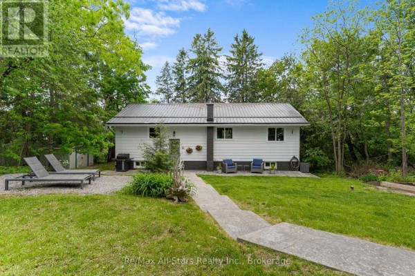 Rear exterior of a white bungalow with a metal roof, surrounded by trees. - 52 Concession Road, Kawartha Lakes