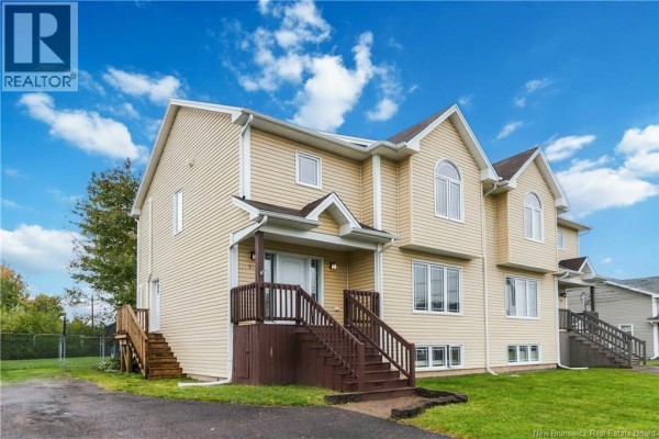 Side exterior view of a beige townhouse showing a dark brown wooden deck and stairs on the left. - 52 Coriander Street, Moncton