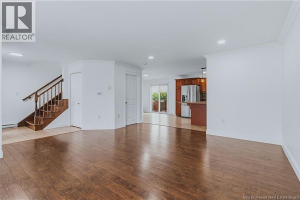 Living room and dining area with white walls, wood floors, a staircase, and a view into the kitchen. - 52 Coriander Street, Moncton