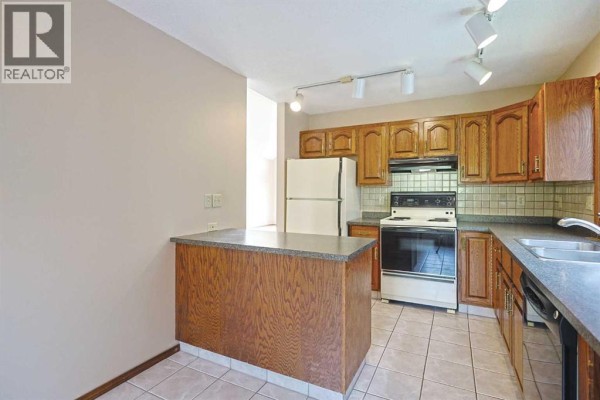 Kitchen with wood cabinets, white appliances, tile floor, and a breakfast bar. - 52 Edgeland Road Nw, Calgary