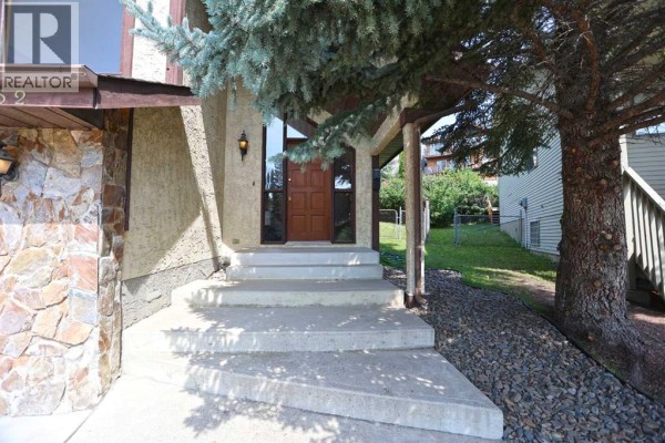 Front entrance with concrete stairs, wooden front door, and stone facade. - 52 Edgeland Road Nw, Calgary
