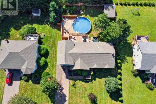 Aerial view of the bungalow's backyard with a wooden deck, above-ground pool, and green lawn. - 52 Hallie Drive, Summerside