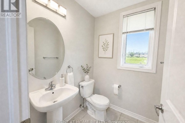 Powder room with a pedestal sink, toilet, oval mirror, and a window overlooking a residential street. - 52 Heming Trail, Hamilton