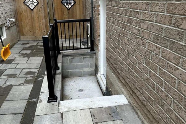 Side yard with stone patio and access to a basement entrance with a black metal railing. - 52 Herefordshire Crescent, Newmarket