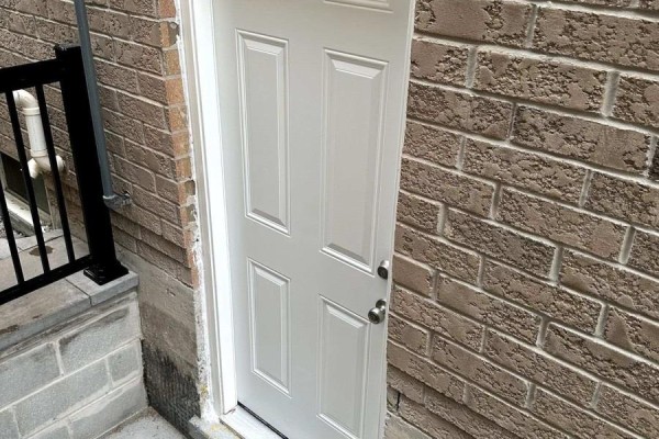 Close-up view of a white exterior door leading to a basement with brick walls. - 52 Herefordshire Crescent, Newmarket