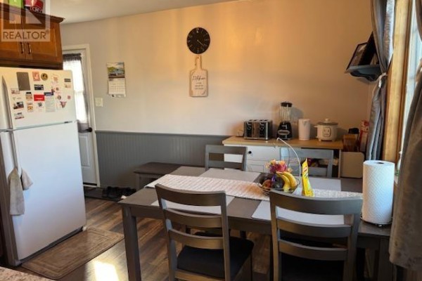A dining area with a table, chairs, refrigerator, and a door to the outside. - 52 Macwilliams Drive, Summerside