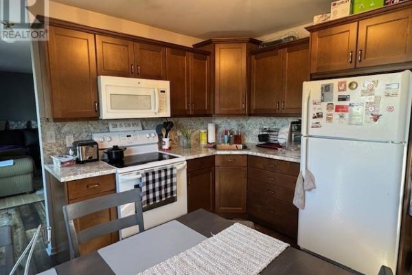 A kitchen with wooden cabinets, white appliances, a stove, and a microwave. - 52 Macwilliams Drive, Summerside