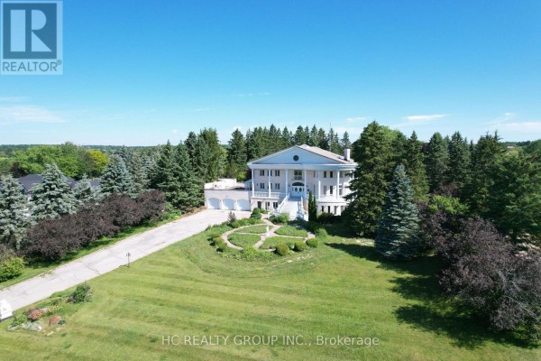 Aerial view of a large white mansion surrounded by mature evergreen trees and a sprawling green lawn. - 52 Nobleton Lakes Drive, King