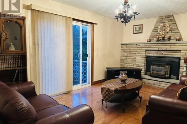 Living room with brown leather couches, a stone fireplace with a gas insert, and vertical blinds. - 52 Norden Cres, Sault Ste  Marie