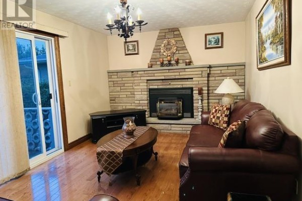 Living room facing the stone fireplace with a dark wood coffee table and brown leather sofa. - 52 Norden Cres, Sault Ste  Marie