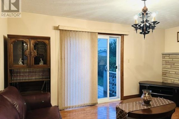 Living room with a large sliding glass door to the outside, a tall wooden cabinet, and brown leather seating. - 52 Norden Cres, Sault Ste  Marie