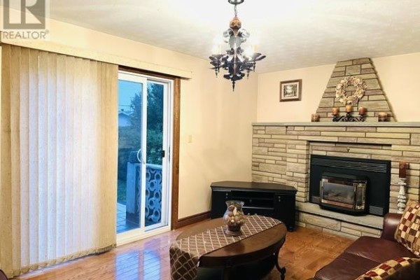 Living room with a stone fireplace, brown leather seating, and a sliding glass door to the backyard. - 52 Norden Cres, Sault Ste  Marie