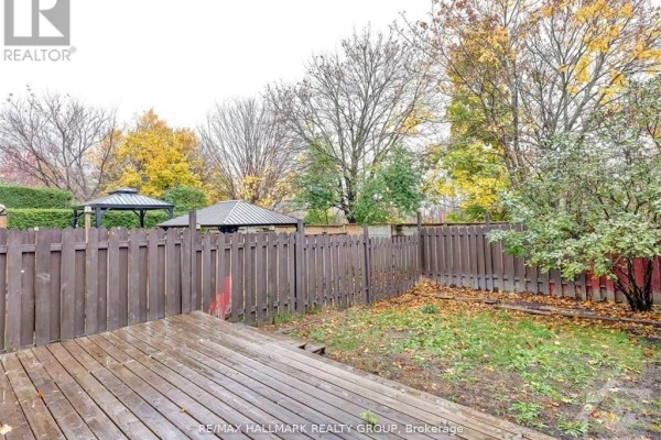 Backyard with a wooden deck, a wooden fence, and mature trees with fall foliage. - 52 Piper Crescent, Ottawa