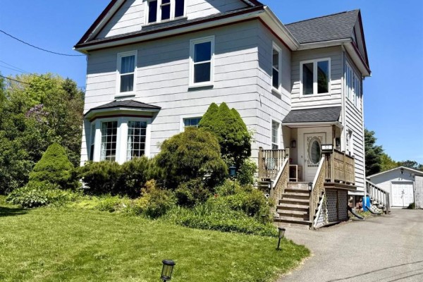 Front exterior of a light grey house with a covered porch, bay window, and asphalt driveway. - 52 Rupert Street, Amherst