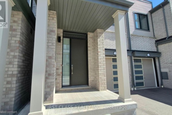 Close-up of a townhouse entrance with a dark grey door, glass sidelight, and beige brick surround. - 52 Sorbara Way, Whitby