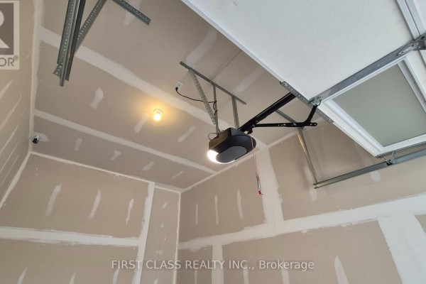 Interior of a garage showing drywall, exposed ceiling beams, and a functional garage door opener. - 52 Sorbara Way, Whitby