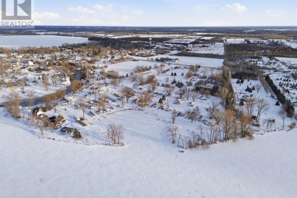 Aerial view of a snowy area with scattered homes and a frozen lake in the background. - 52 Sunset Lagoon Drive, Prince Edward County