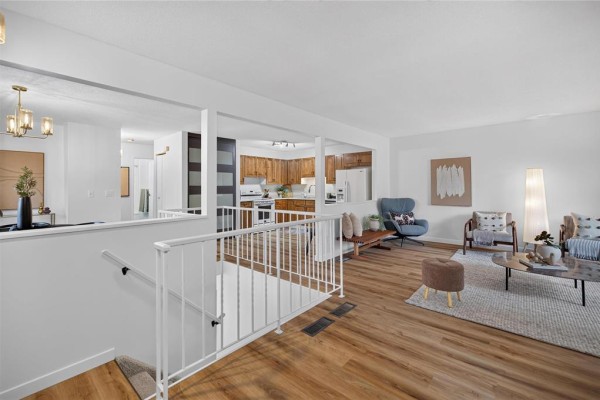Open-concept living area with wood-look flooring, white walls, and a view of the kitchen. - 52 Trowbridge Bay, Winnipeg
