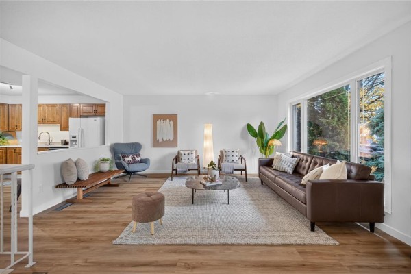 Living room with a brown leather sofa, coffee table, and large window overlooking the yard. - 52 Trowbridge Bay, Winnipeg