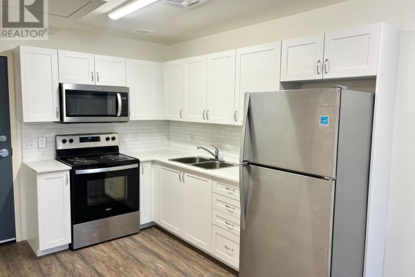 Corner kitchen with white cabinets, stainless steel appliances, and subway tile backsplash. - 520 - 135 Station Street, Belleville
