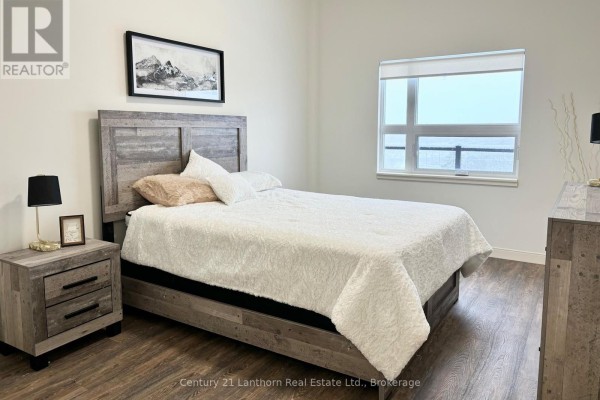 Bedroom with queen bed, wooden furniture, and a large window. - 520 - 135 Station Street, Belleville