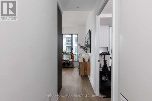Interior hallway with light wood floors, white walls, and doorways to living room and exercise room. - 520 - 280 Howland Avenue, Toronto