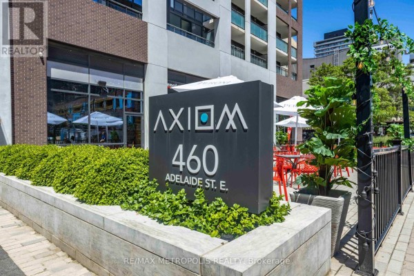 Building entrance with a glass canopy, modern paving, and greenery. - 520 - 460 Adelaide Street E, Toronto