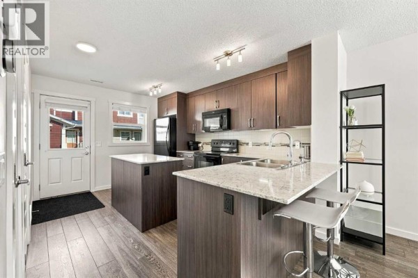 Kitchen with dark wood cabinets, granite countertops, island, and back door. - 520 Auburn Bay Circle Se, Calgary