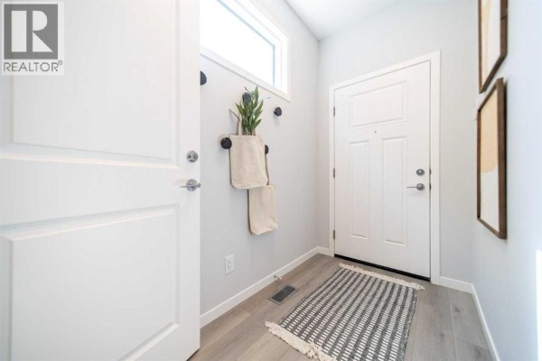 Entrance foyer with white doors, light wood flooring, and a grey and white striped rug. - 520 Tekarra Drive Nw, Calgary