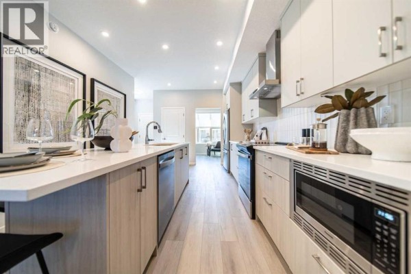 Long, modern kitchen with light wood lower cabinets, white upper cabinets, and stainless steel appliances. - 520 Tekarra Drive Nw, Calgary