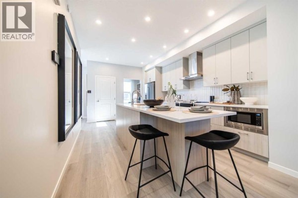 Modern kitchen with a large island, two black stools, light wood cabinets, and white countertops. - 520 Tekarra Drive Nw, Calgary