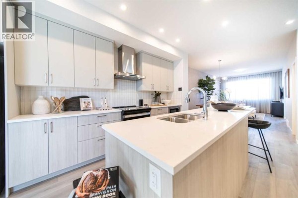 Kitchen with a large island, stainless steel appliances, light wood cabinets, and a view of the living area. - 520 Tekarra Drive Nw, Calgary