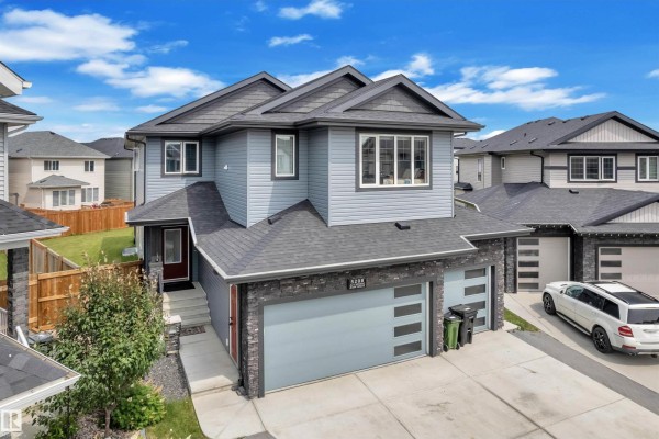 Front view of a grey duplex with stone base, large garage doors, and windows. - 5208 23a Av Sw, Edmonton