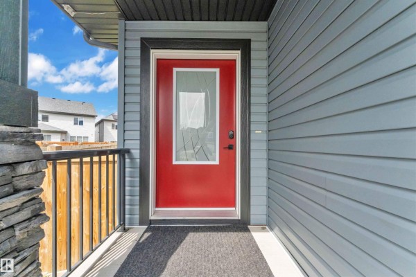 Close-up of a red front door with glass insert and grey siding. - 5208 23a Av Sw, Edmonton