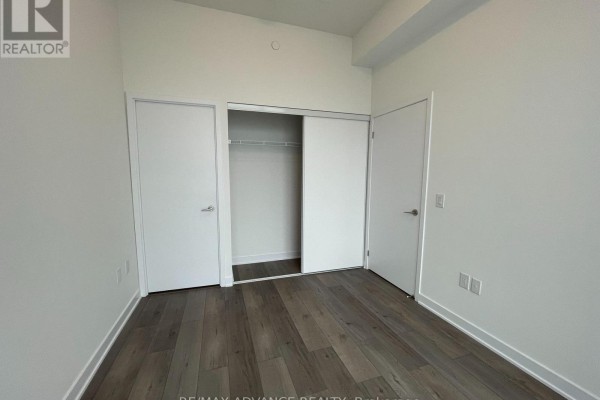 Bedroom with two white doors and sliding closet doors, featuring wood plank flooring. - 521 - 10 Honeycrisp Crescent, Vaughan