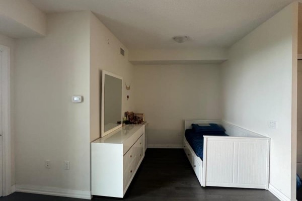Bright bedroom with a white dresser, mirror, and a twin bed against a white wall. - 521 - 50 Thomas Riley Road, Toronto