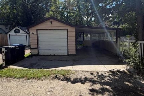 Attached single-car garage with a light beige overhead door and an adjacent carport. - 521 17th Street, Brandon