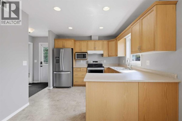 Kitchen with light wood cabinets, stainless steel appliances, and a U-shaped counter with an island. - 521 Partridge Crescent, Pelican Point
