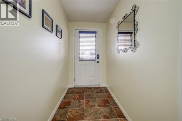 Interior hallway with wood laminate flooring, a staircase with wooden railings, and a view of the living area. - 521 Snowdrop Court, Kitchener