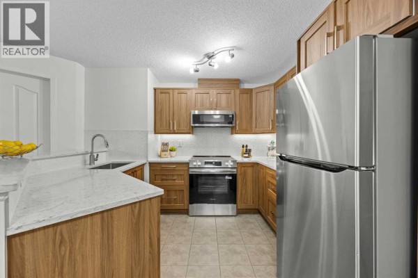 L-shaped kitchen features wood cabinets, stainless steel appliances, and white tiled backsplash. - 5210, 16969 24 Street Sw, Calgary