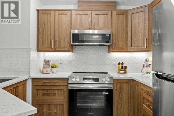 Detail of a stainless steel oven and range with wood cabinetry and white hexagon tile backsplash. - 5210, 16969 24 Street Sw, Calgary