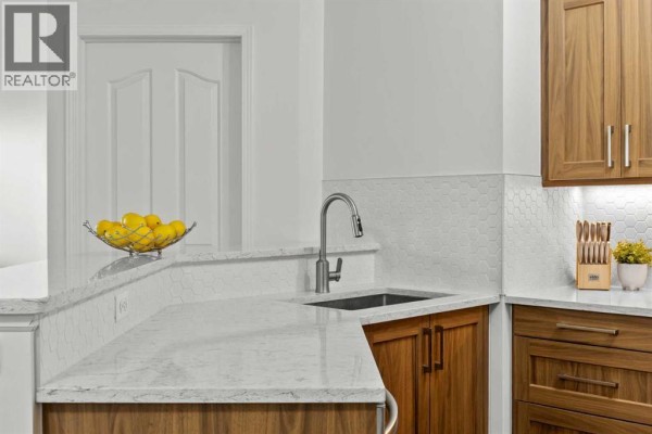 Kitchen counter area with sink, faucet, granite countertop, and white hexagonal tile backsplash. - 5210, 16969 24 Street Sw, Calgary